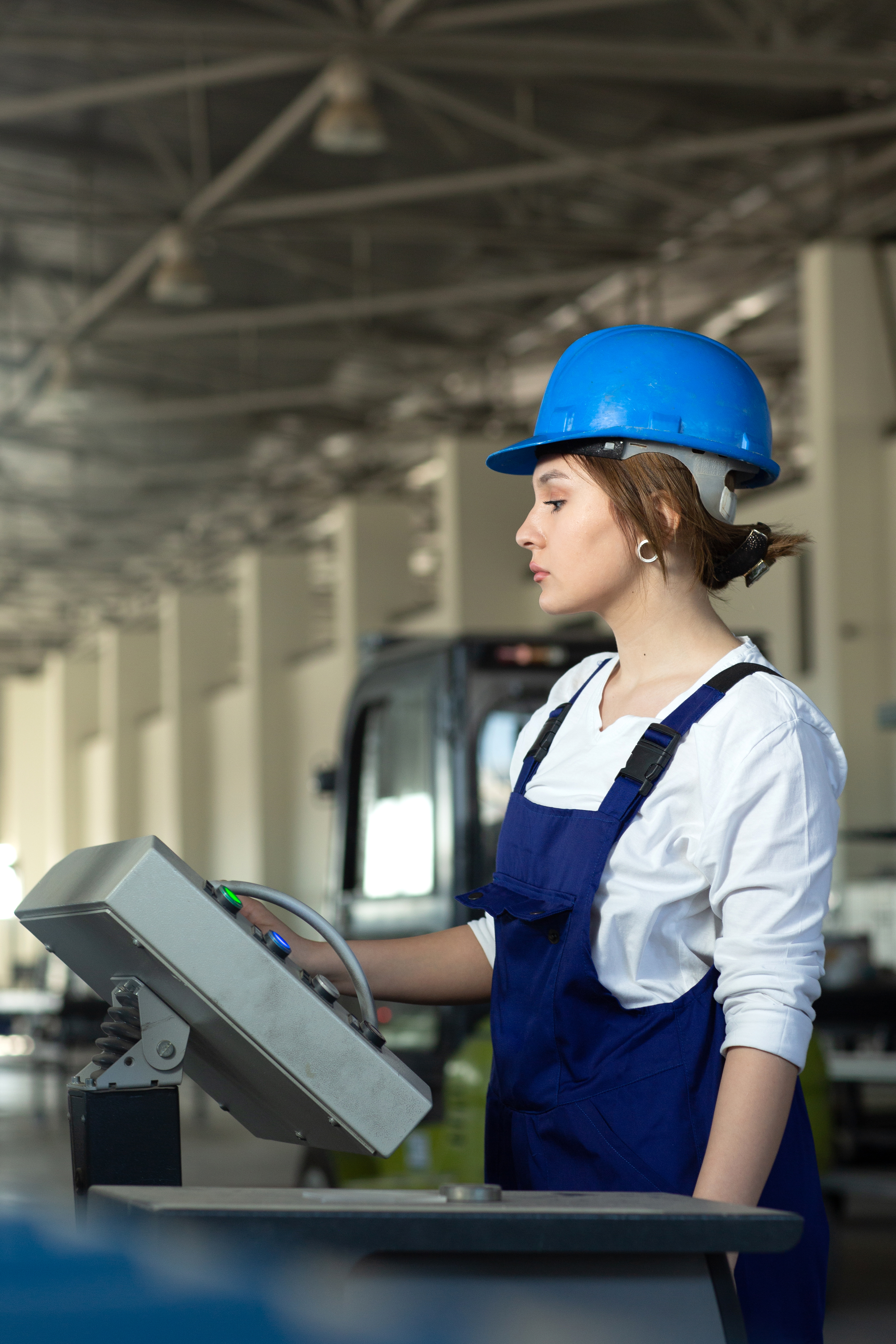 front-view-young-attractive-lady-blue-construction-suit-helmet-controlling-machines-hangar-working-during-daytime-buildings-architecture-construction