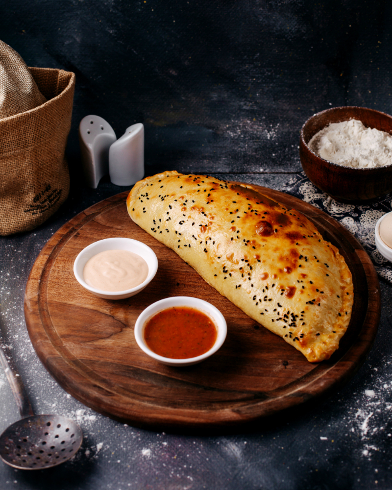 front-view-cooked-pastry-along-with-red-white-sauces-brown-wooden-round-desk-grey-floor