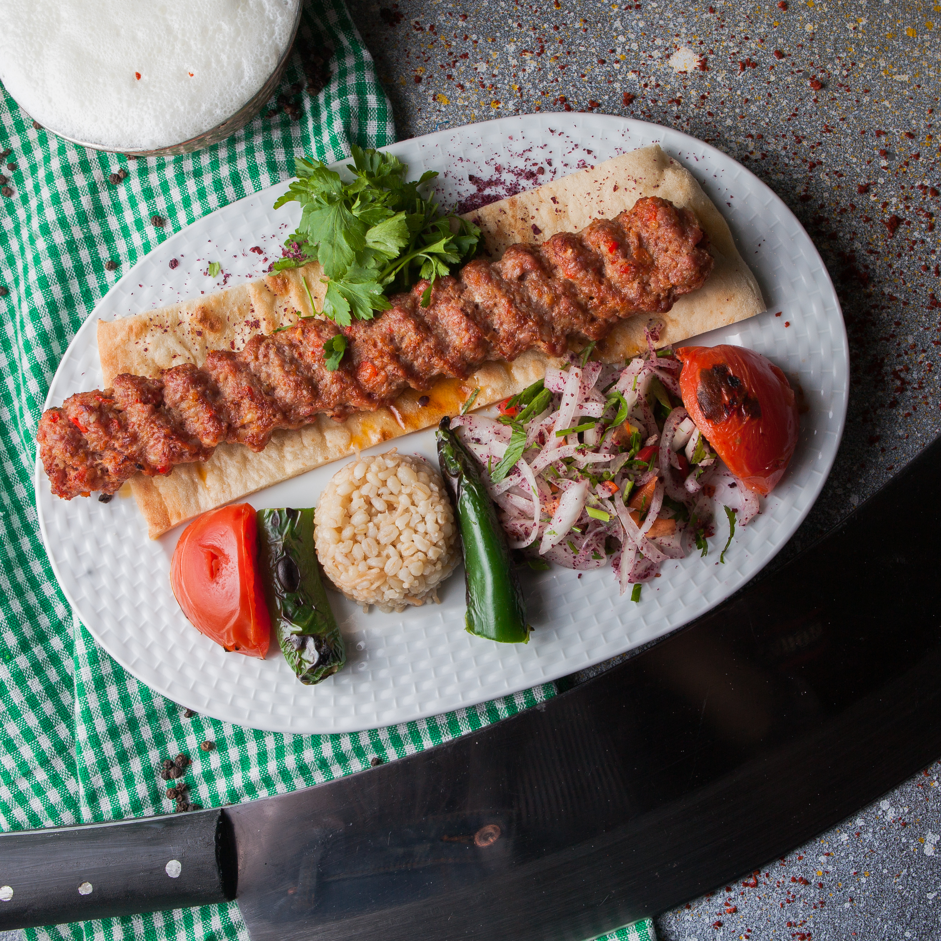 top-view-adana-kebab-with-rice-fried-vegetables-chopped-onion-ayran-white-plate